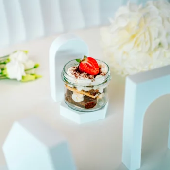 Mini tiramisu w szklanym słoiczku z kremem mascarpone, kakao i truskawką, podane w eleganckiej aranżacji